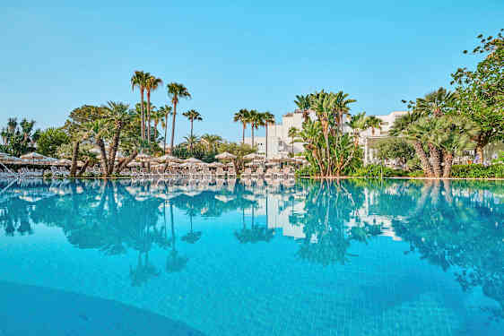 Udendørs pool omgivet af liggestole og palmer. (AI-genereret tekst)