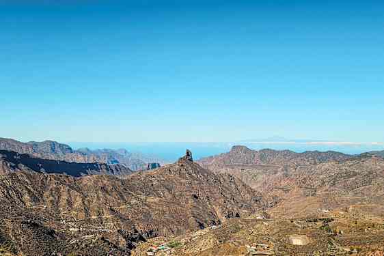 Landskab med bjerge og en markant klippeformation under blå himmel. (AI-genereret tekst)