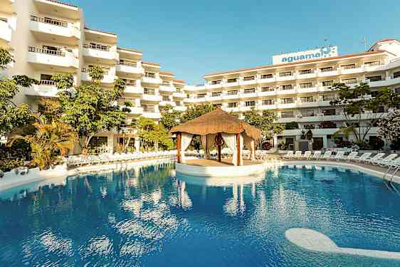 Hotelkompleks med flere etager, en stor pool og en tagehytte struktur midt i poolen. (AI-genereret tekst)