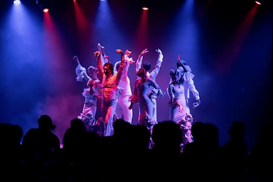 Dansere optræder med en koreografi på en scene med farvet lyssætning. (AI-genereret tekst)