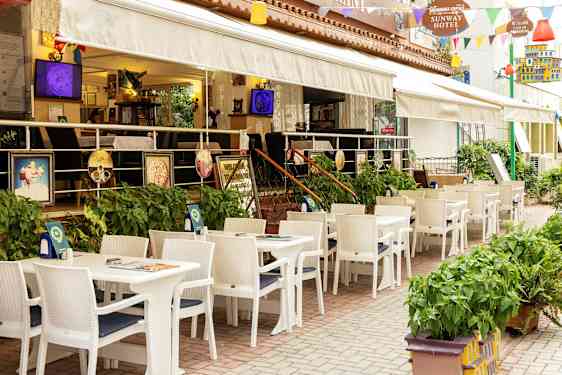 Restaurant med udendørs servering med hvide borde og stole ved et hotel. (AI-genereret tekst)