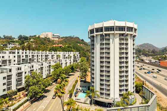 En moderne høj bygning omgivet af veje, grønne områder og andre bygninger. (AI-genereret tekst)