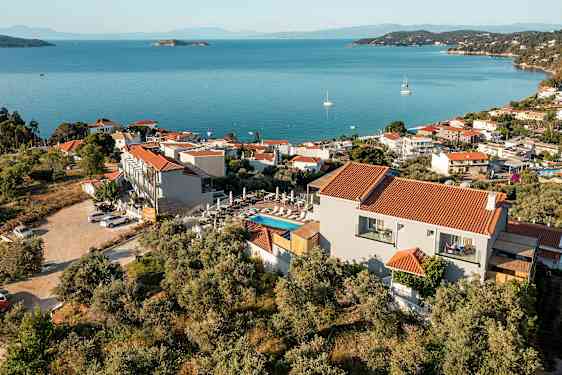 En udsigt over en kystby med røde tage på hvide bygninger, omgivet af grønne områder og med det blå hav i baggrunden. (AI-genereret tekst)