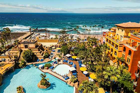 Et hotelområde med pools, beplantning og farverige bygninger ved havet. (AI-genereret tekst)