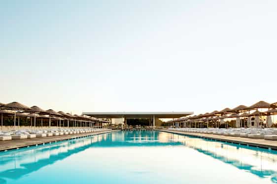 En stor og lang pool med parasoller og liggestole på begge sider. (AI-genereret tekst)