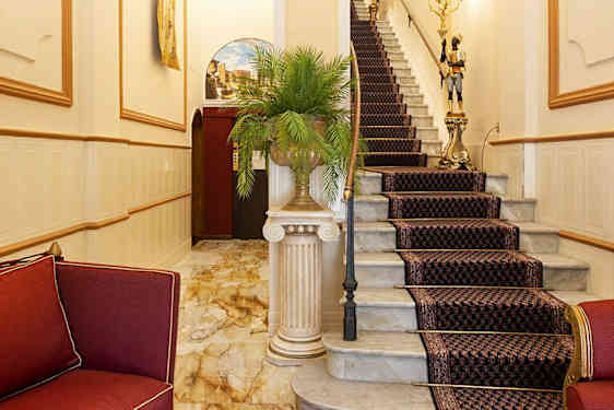 Elegant foyer med røde møbler og en trappe med mønstret tæppe. (AI-genereret tekst)