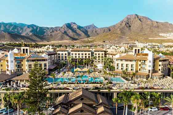 Hotelbygninger med poolområde og bjerge i baggrunden. (AI-genereret tekst)