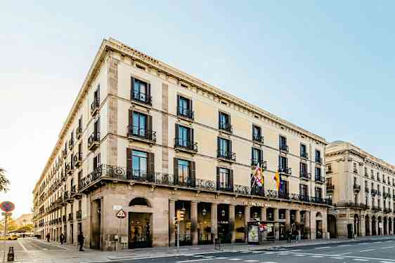 Et gadehjørne med en bygning i klassisk stil, der har flere etager, buer og dekorerede altaner. (AI-genereret tekst)