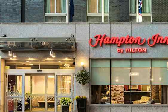 Hotelindgang med skiltet "Hampton Inn by Hilton" over dørene. (AI-genereret tekst)