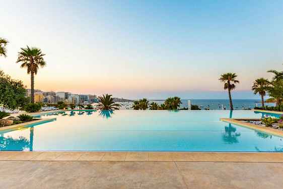 Infinitypool med udsigt over havet, omgivet af palmer og grønne områder. (AI-genereret tekst)