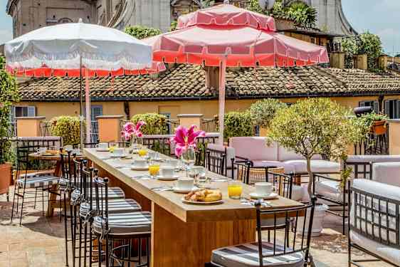 En terrasse med siddegrupper, morgenmad serveret og parasoller i solskinsvejr. (AI-genereret tekst)