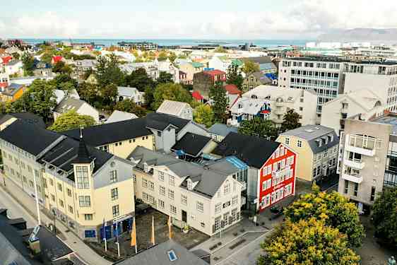 En byudsigt med farverige bygninger, træer og en vej, samt baggrund med hav og bjerge. (AI-genereret tekst)