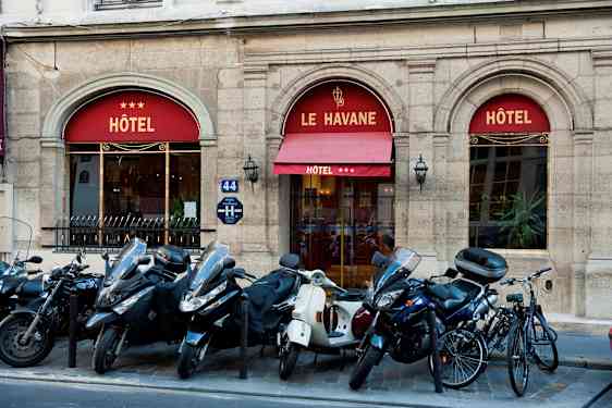 Billede, der viser indgangen til et hotel med navnet Le Havane, tre stjerner vises på markisen. Foran bygningen er der parkeret scootere og cykler. (AI-genereret tekst)