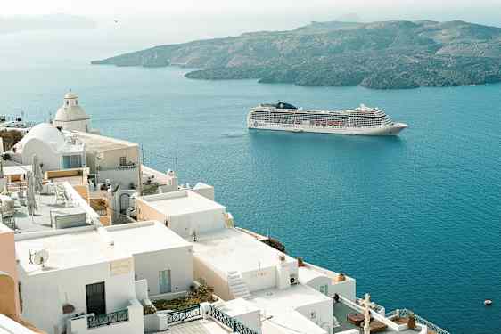 Et krydstogtskib sejler forbi hvide bygninger ved kysten. (AI-genereret tekst)