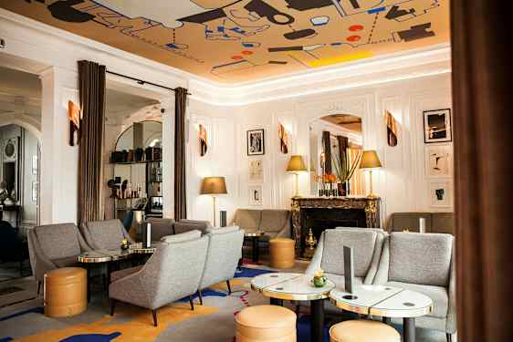 Et elegant opholdsstue med grå sofaer og stole, marmorborde, en dekorativ pejs og kunst på væggen. (AI-genereret tekst)