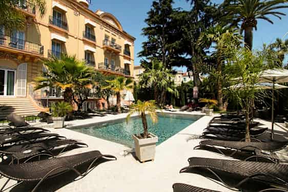 En udendørs pool ved et hotel omgivet af palmer og liggestole. (AI-genereret tekst)