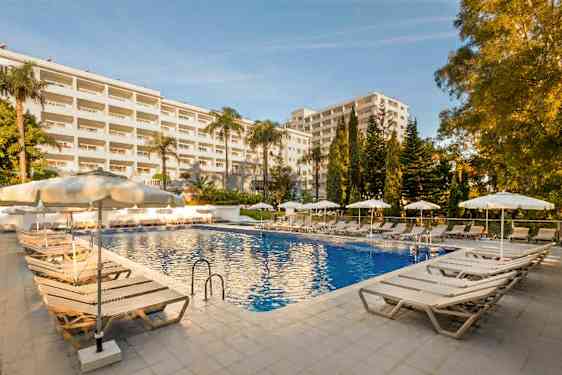 Billede af en udendørs swimmingpool ved et hotel omgivet af liggestole og parasoller. (AI-genereret tekst)