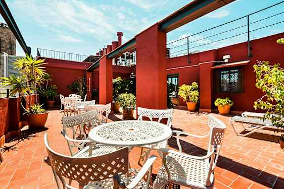 En terrasse med hvide metalmøbler og potteplanter på et terracottaflisegulv, omgivet af rødmalede vægge. (AI-genereret tekst)