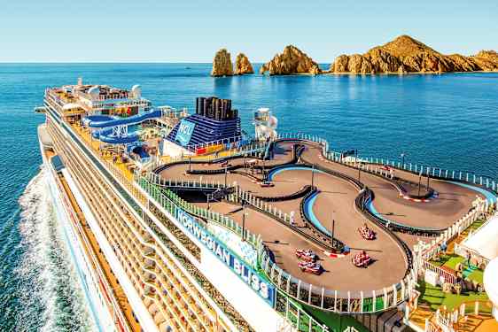 Et krydstogtskib med en gokartbane på dækket, omgivet af havet og klippelandskab i baggrunden. (AI-genereret tekst)