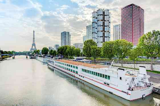 Flod med en båd ved kaj, moderne bygninger og Eiffeltårnet i baggrunden. (AI-genereret tekst)