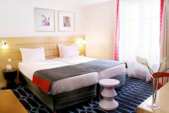 Et hotelværelse med to enkeltsenge, et dekorativt sengegærde og et vindue med lysindfald. (AI-genereret tekst)