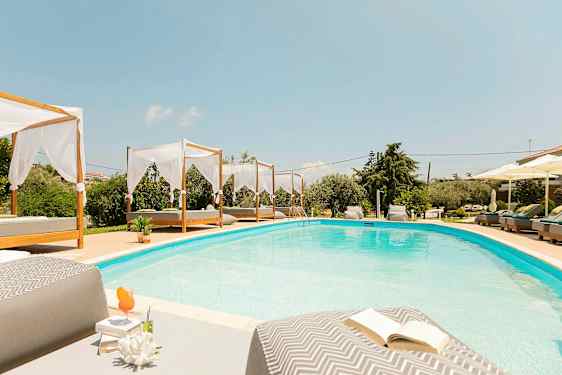 En swimmingpool med senge og parasoller rundt om. (AI-genereret tekst)