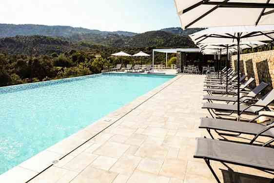 En infinitypool med liggestole og parasoller ved siden af, beliggende med udsigt over et naturskønt bjerglandskab. (AI-genereret tekst)