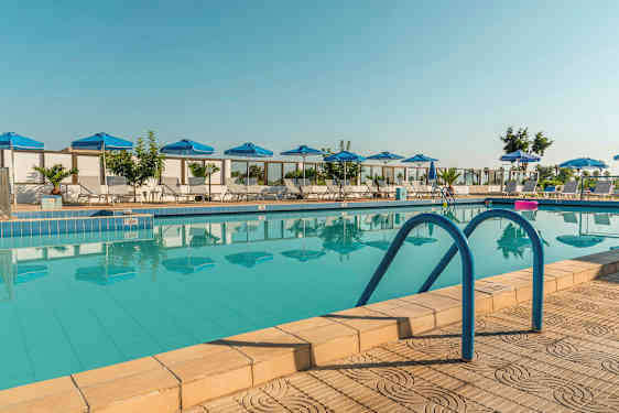 Et billede af en udendørs pool med blå parasoller og liggestole rundt omkring. (AI-genereret tekst)