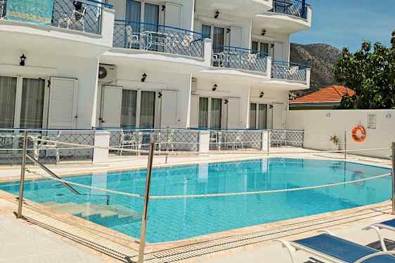 Billede af en pool foran et hvidmalet hotel med blå balkoner og liggestole ved poolen. (AI-genereret tekst)