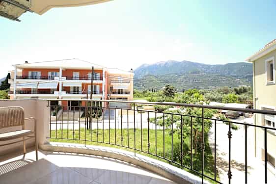 Udsigt fra en altan med en stol, en græsplæne og bygninger i baggrunden. (AI-genereret tekst)