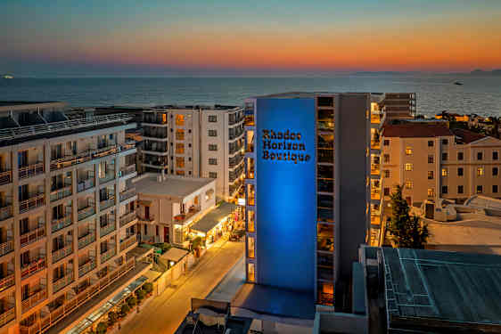 Udsigt over et hotelområde med havet i baggrunden ved solnedgang. (AI-genereret tekst)