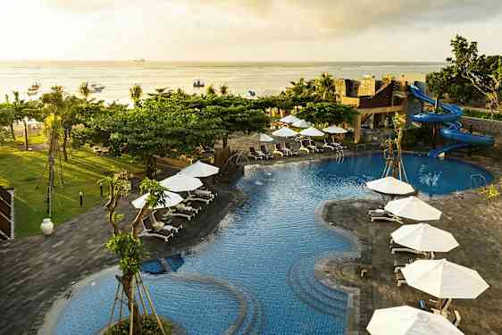 Billedet viser et poolområde med blåt vand, omgivet af solsenge og hvide parasoller. Der er en vandrutsjebane og udsigt over havet. (AI-genereret tekst)