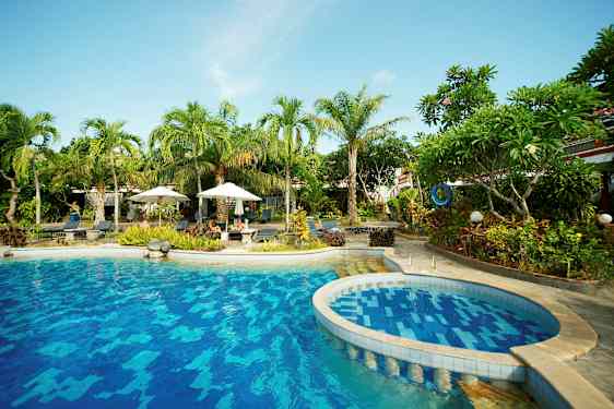 Billede af en udendørs pool omgivet af tropiske palmer og planter. (AI-genereret tekst)