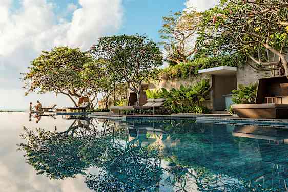 Pool nær frodige træer og komfortable liggestole. (AI-genereret tekst)