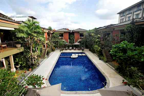 En udendørs swimmingpool omgivet af planter og bygninger. (AI-genereret tekst)