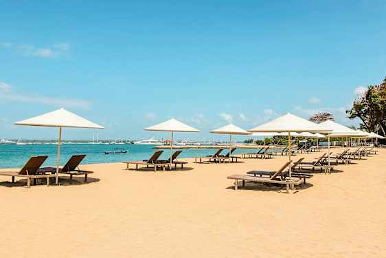 Strand med liggestole under parasoller ved havet. (AI-genereret tekst)