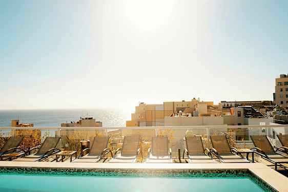 En pool med solsenge foran en udsigt over havet og bygninger. (AI-genereret tekst)