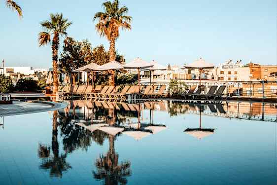 En pool med parasoller og liggestole på en solrig dag. (AI-genereret tekst)