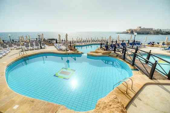 Billede af en udendørs pool ved stranden med liggestole og parasoller omkring. (AI-genereret tekst)