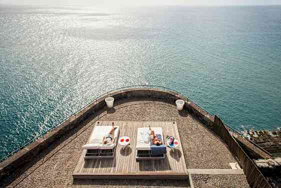 En terrasse med to solsenge og havet i baggrunden. (AI-genereret tekst)