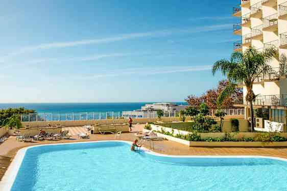 En udendørs swimmingpool med liggestole og en klar blå himmel over havet. (AI-genereret tekst)