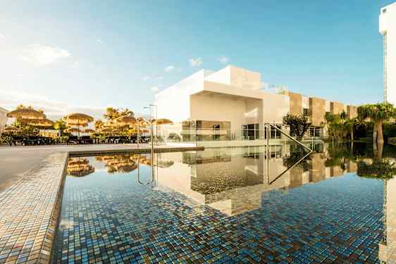 Poolområde med parasoller og hvide bygninger. (AI-genereret tekst)