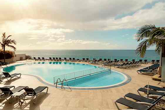 Udendørs pool med liggestole omkring, beliggende tæt på havet under en klar himmel. (AI-genereret tekst)