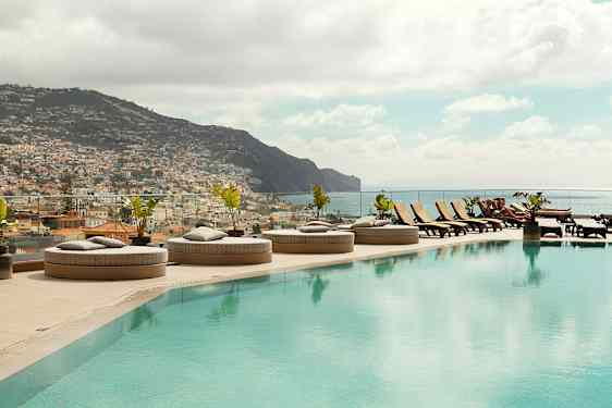 En infinitypool med liggestole og udsigt over en by og bjerge. (AI-genereret tekst)