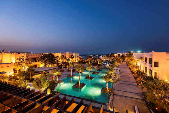 Et oplyst feriested med pools og palmer om aftenen. (AI-genereret tekst)