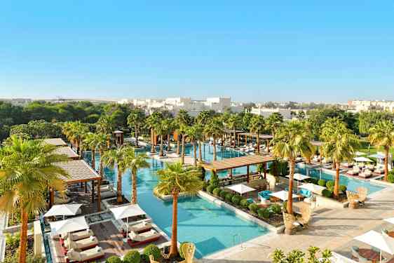 Et luksuriøst poolområde omgivet af grønne områder og palmer, med liggestole og parasoller. (AI-genereret tekst)