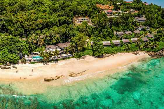 Strand med turkis vand, omgivet af frodig vegetation og bygninger. (AI-genereret tekst)