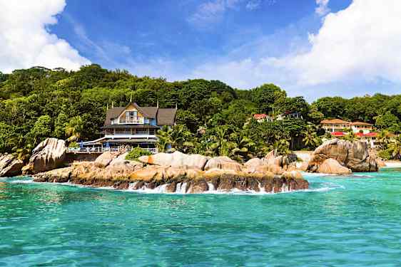 Strand med klipper foran en bygning omgivet af grønne områder. (AI-genereret tekst)