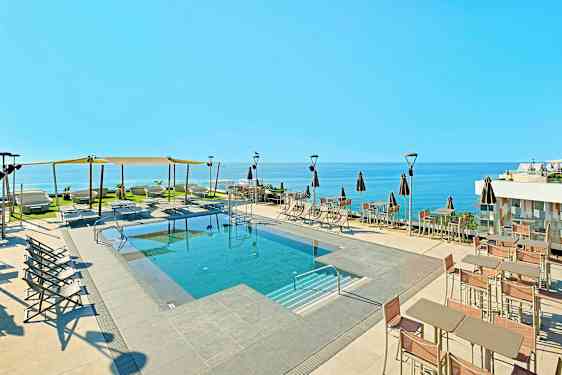 Udendørs pool med liggestole og parasoller samt havudsigt. (AI-genereret tekst)