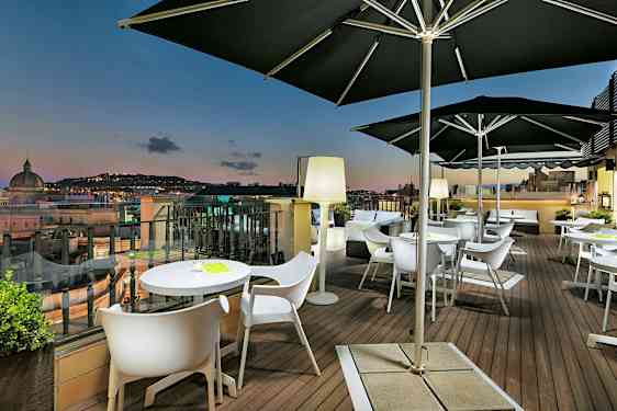 En terrasse med borde og stole samt udsigt over en by i skumringen. (AI-genereret tekst)